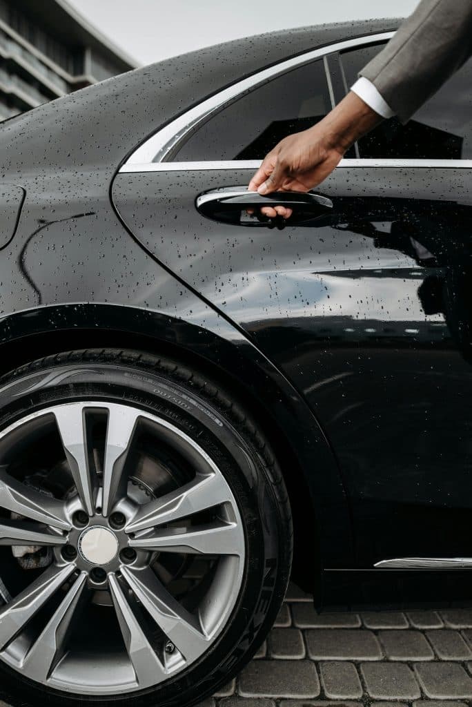 A chauffeur opening the door of a black S class Mercedes