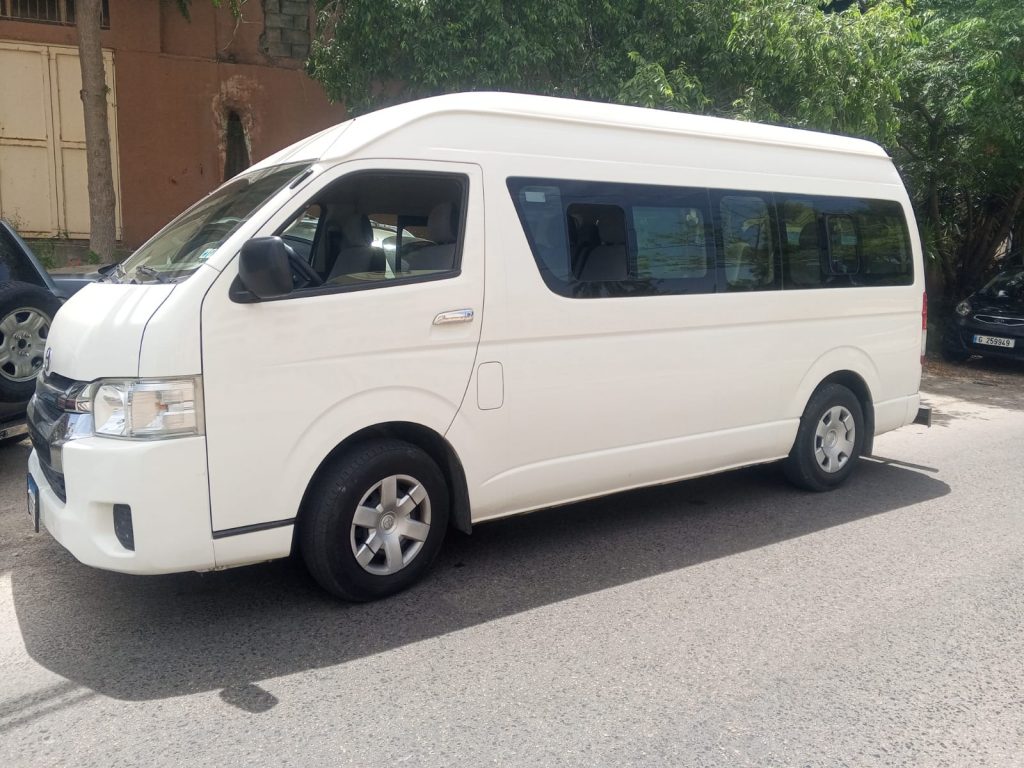 A white Toyota Hiace from the side in front of large green tree